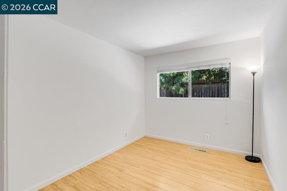 Empty room with light wood-look flooring, a wide window, and a floor lamp.