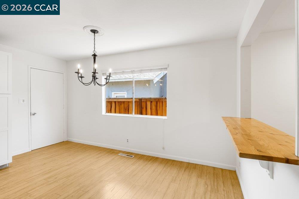 Empty dining area with a dark chandelier, light wood floors, and a wood countertop.