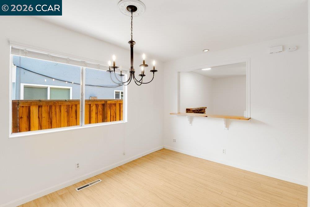 Empty dining room with a chandelier, light wood floors, large window, and pass-through counter.