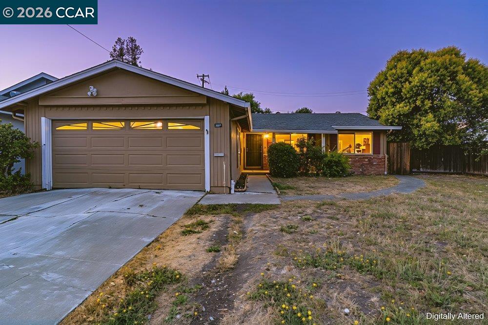Single-story home at dusk with a two-car garage, concrete driveway, and warmly lit windows.