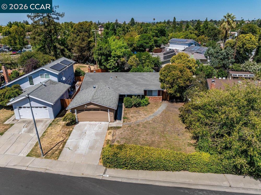 Aerial view of a single-story home with an attached garage, broad driveway, and dry front yard.