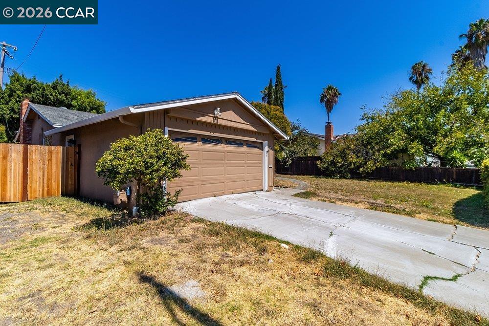 Single-story home with a tan double garage, wide concrete driveway, and dry front lawn.