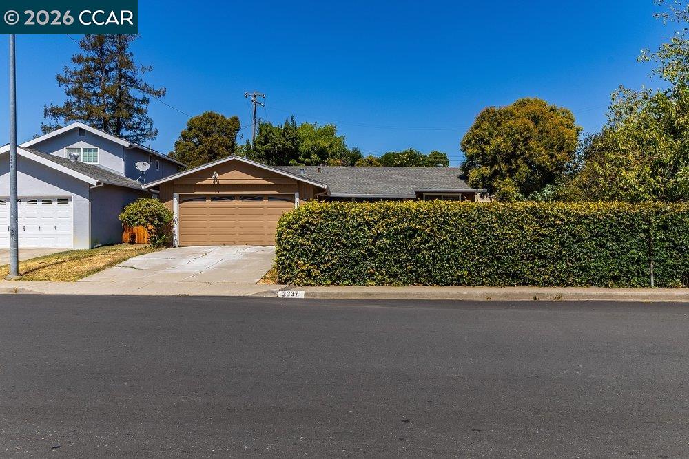 Single-story home with a tan double garage door and tall hedge along the front.