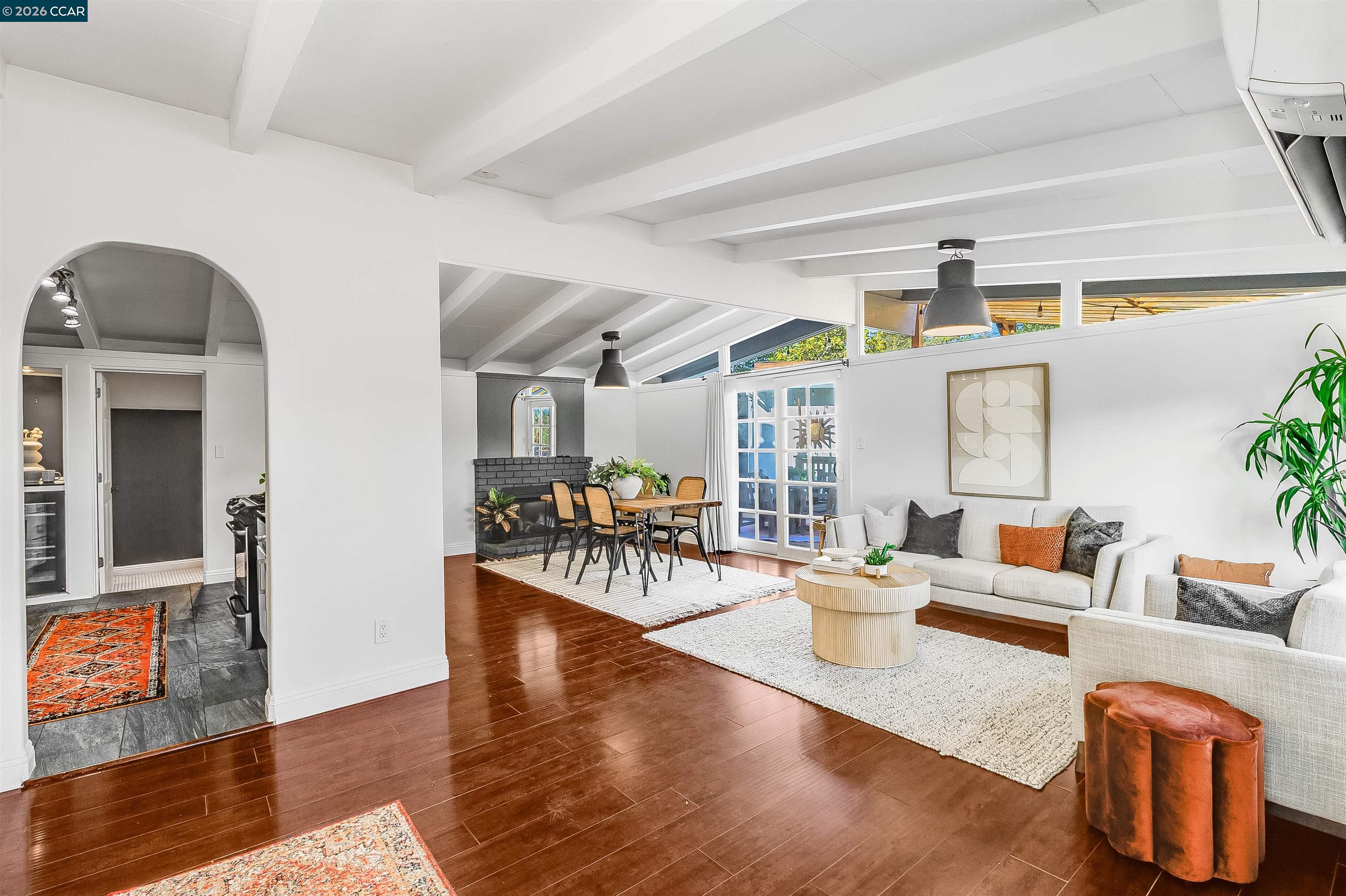 Open-plan living and dining room with a beamed ceiling, black brick fireplace, and dark hardwood floors.
