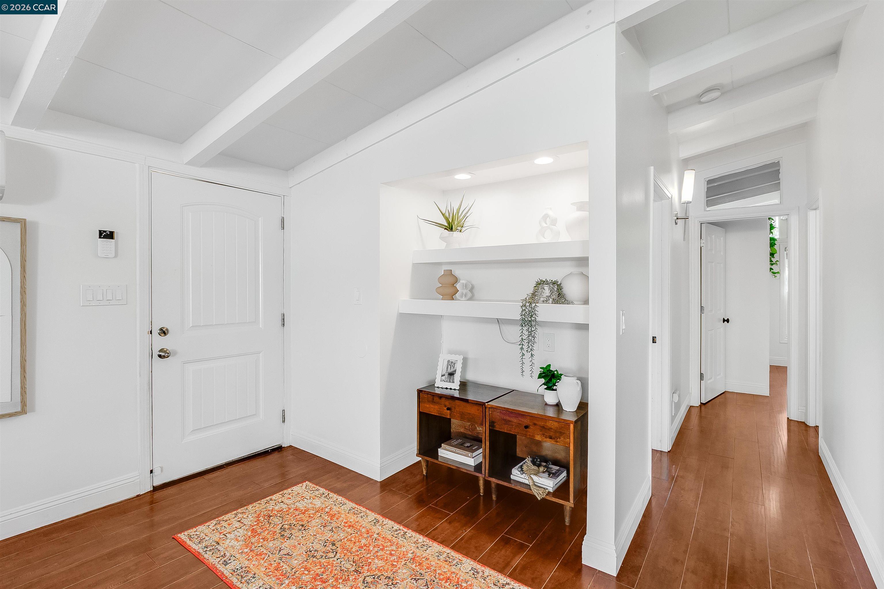 Staged entry foyer with built-in display shelves, a vaulted beam ceiling, and dark wood floors.