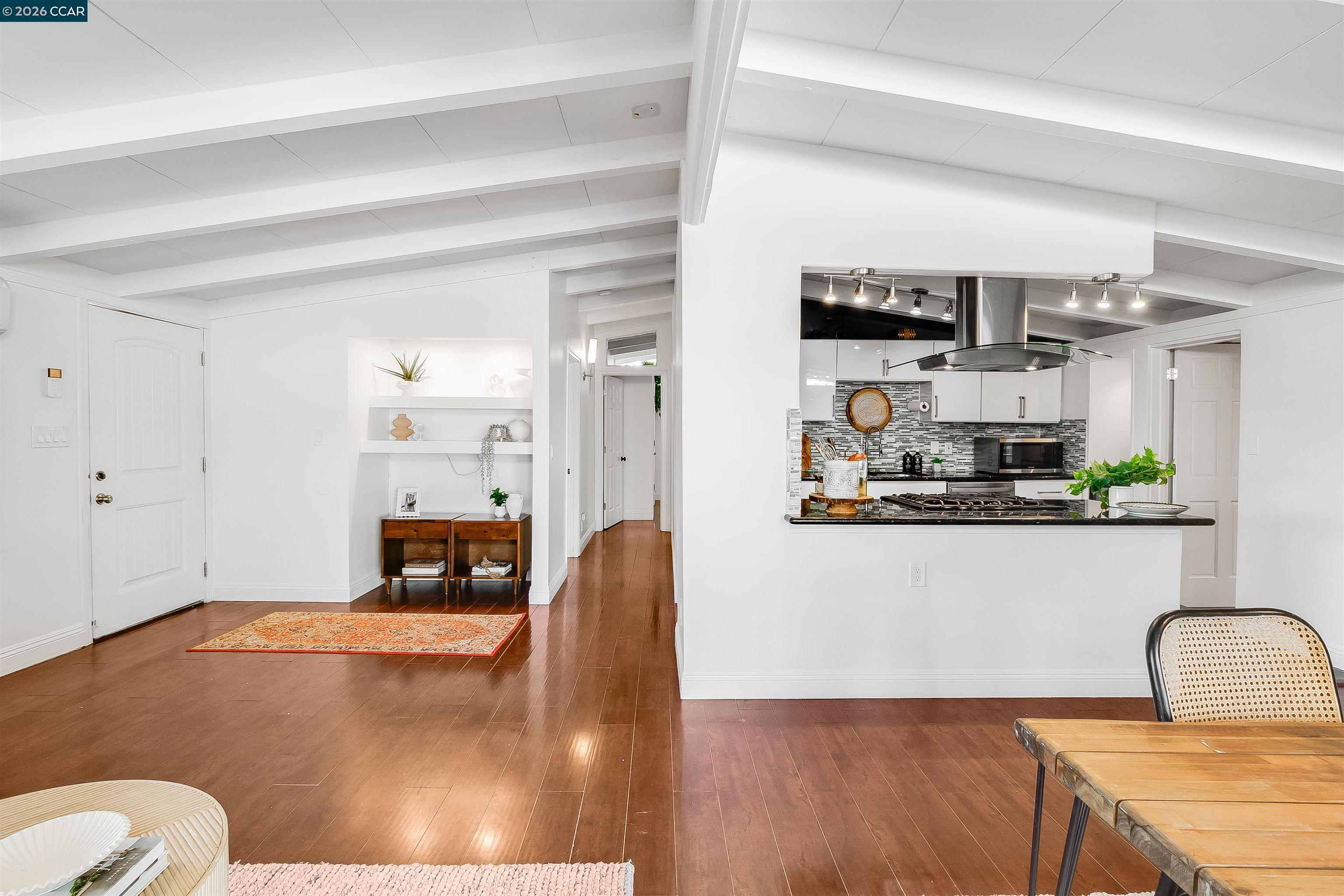 Open-plan kitchen with a mosaic backsplash, stainless range hood, and warm wood floors.