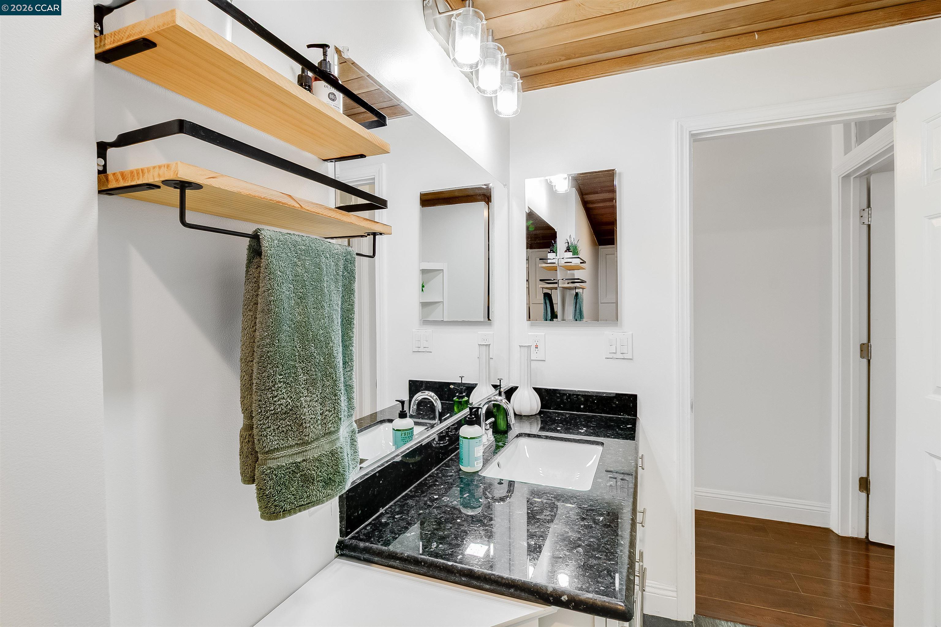 Bathroom vanity with black stone counters, double sinks, and open wooden towel shelves.