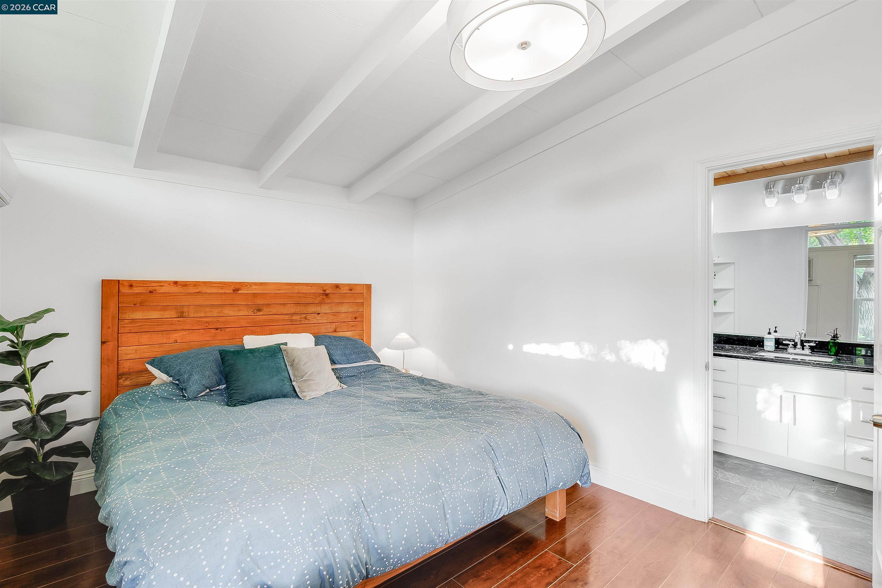 Bedroom with a blue patterned bedspread and wood plank headboard, opening to an adjoining bathroom.