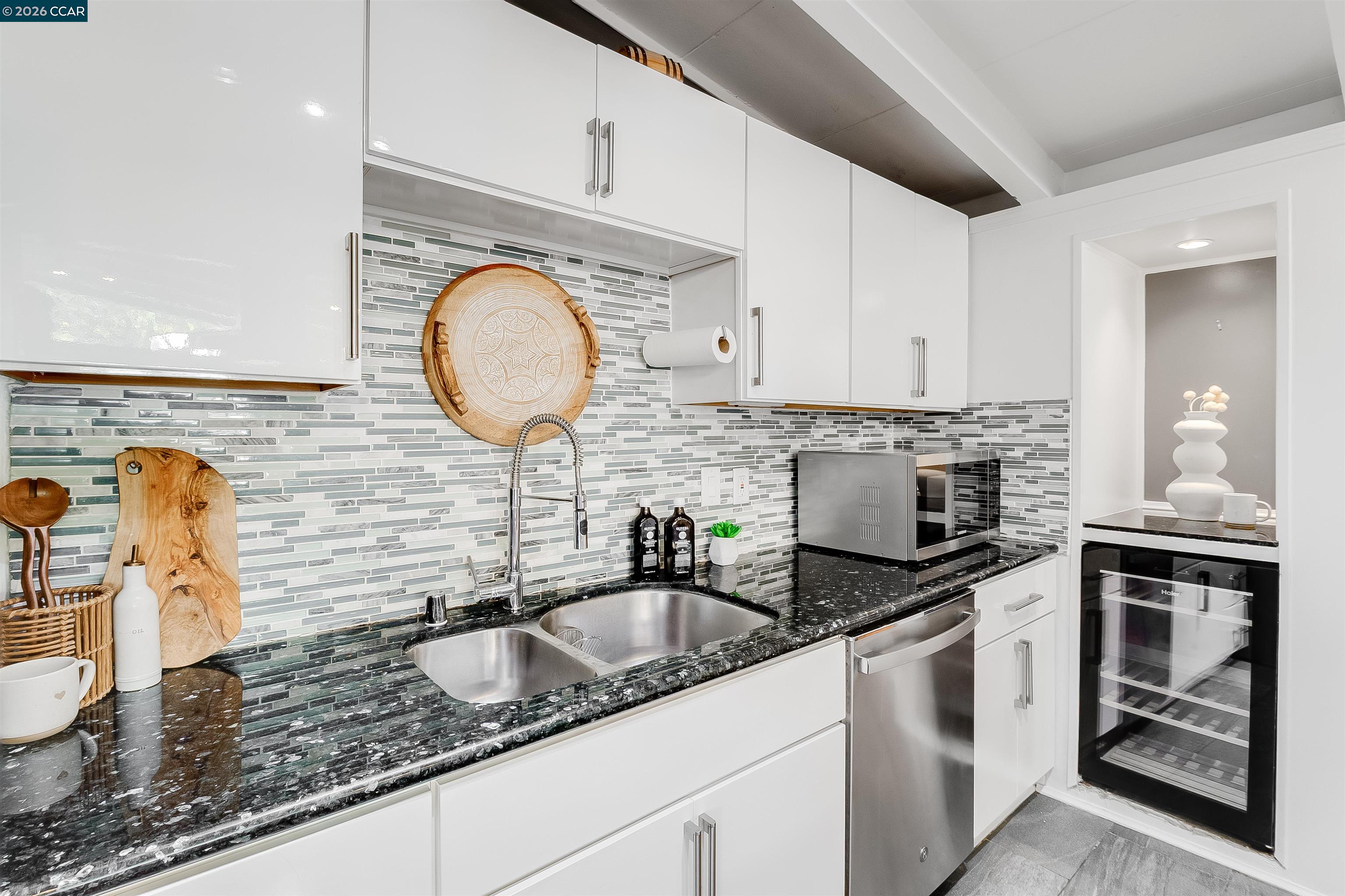 Kitchen with white cabinetry, mosaic tile backsplash, dark countertops, and a glass-front wine refrigerator.