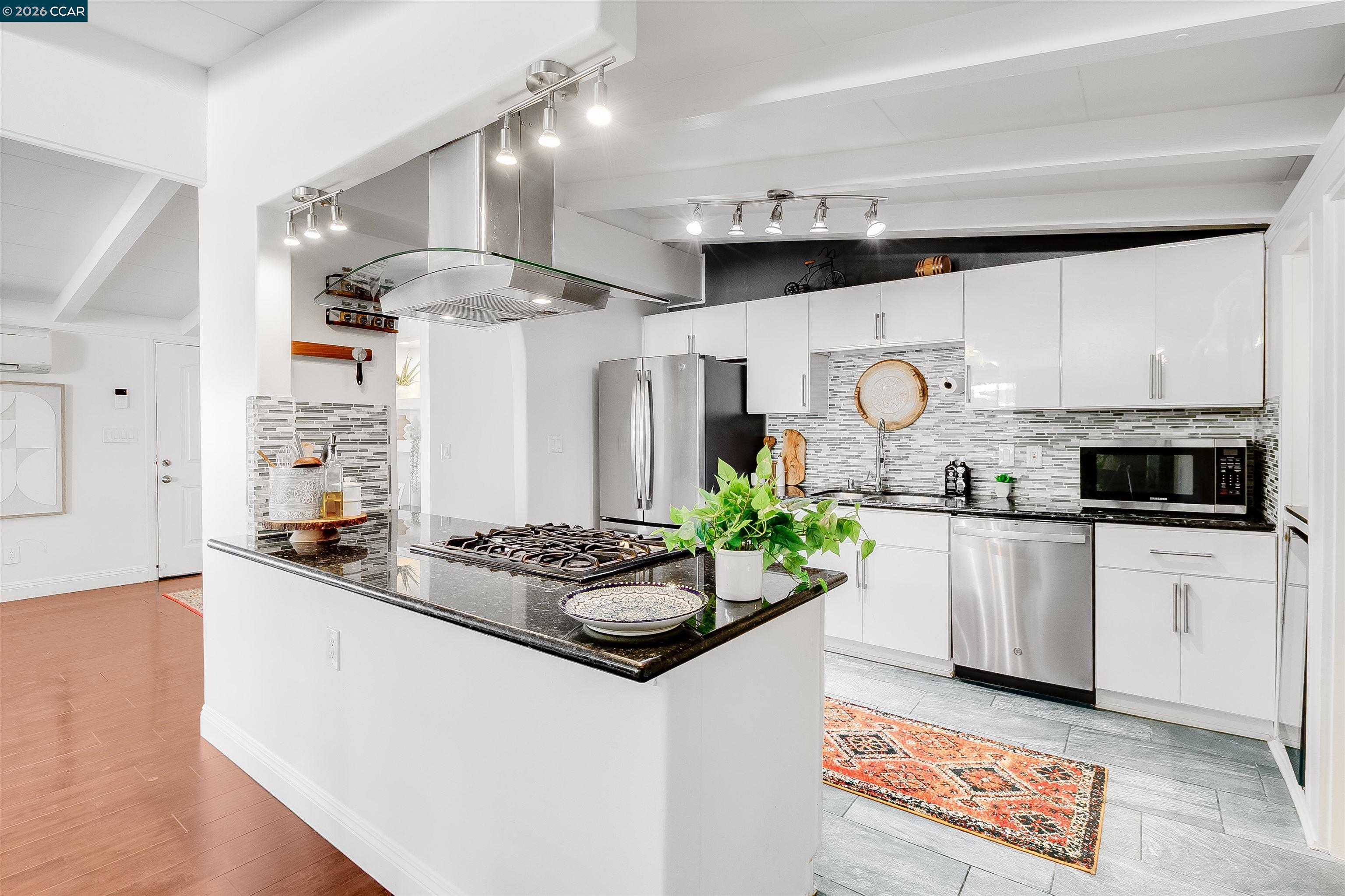 Bright white kitchen with stainless steel appliances, mosaic backsplash, and a black island with gas cooktop.
