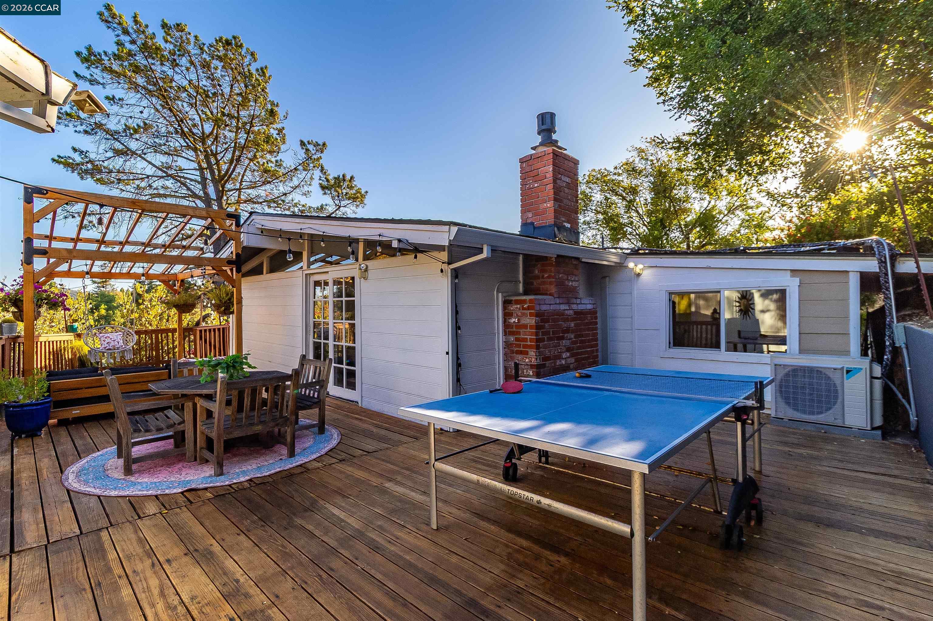 Wooden backyard deck with a pergola dining area, blue ping-pong table, and brick chimney.