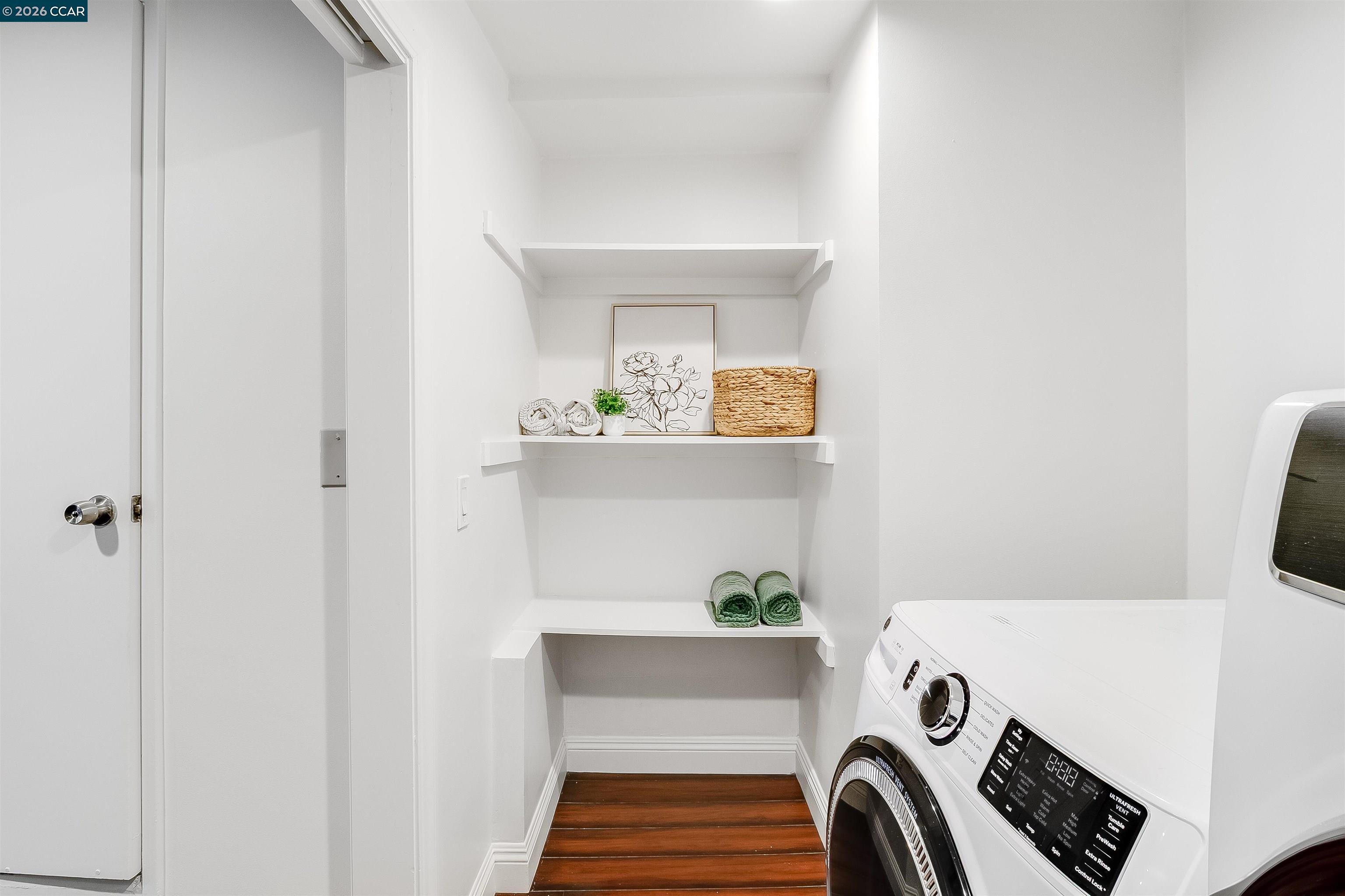 Laundry room with front-loading appliances, decorated built-in shelves, and dark wood flooring.