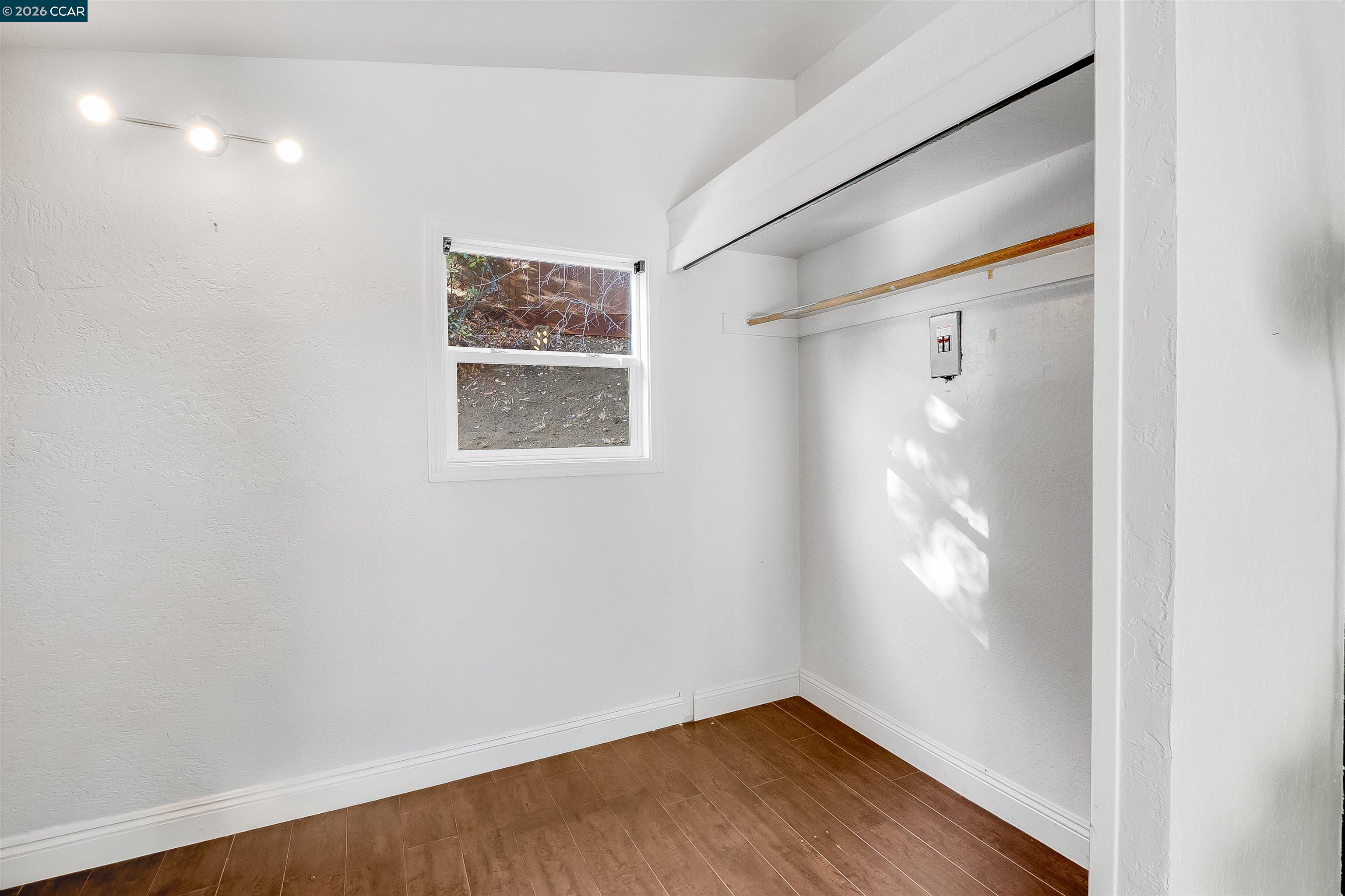 Empty closet with a built-in hanging rod, shelf, small window, and brown wood-look flooring.