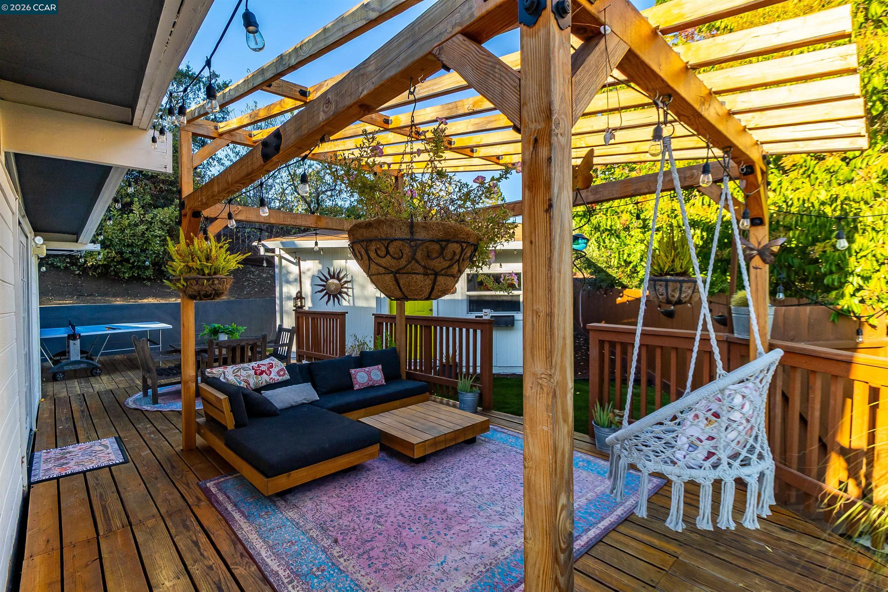 Outdoor patio beneath a wooden pergola, furnished with a sectional sofa and hanging swing chair.