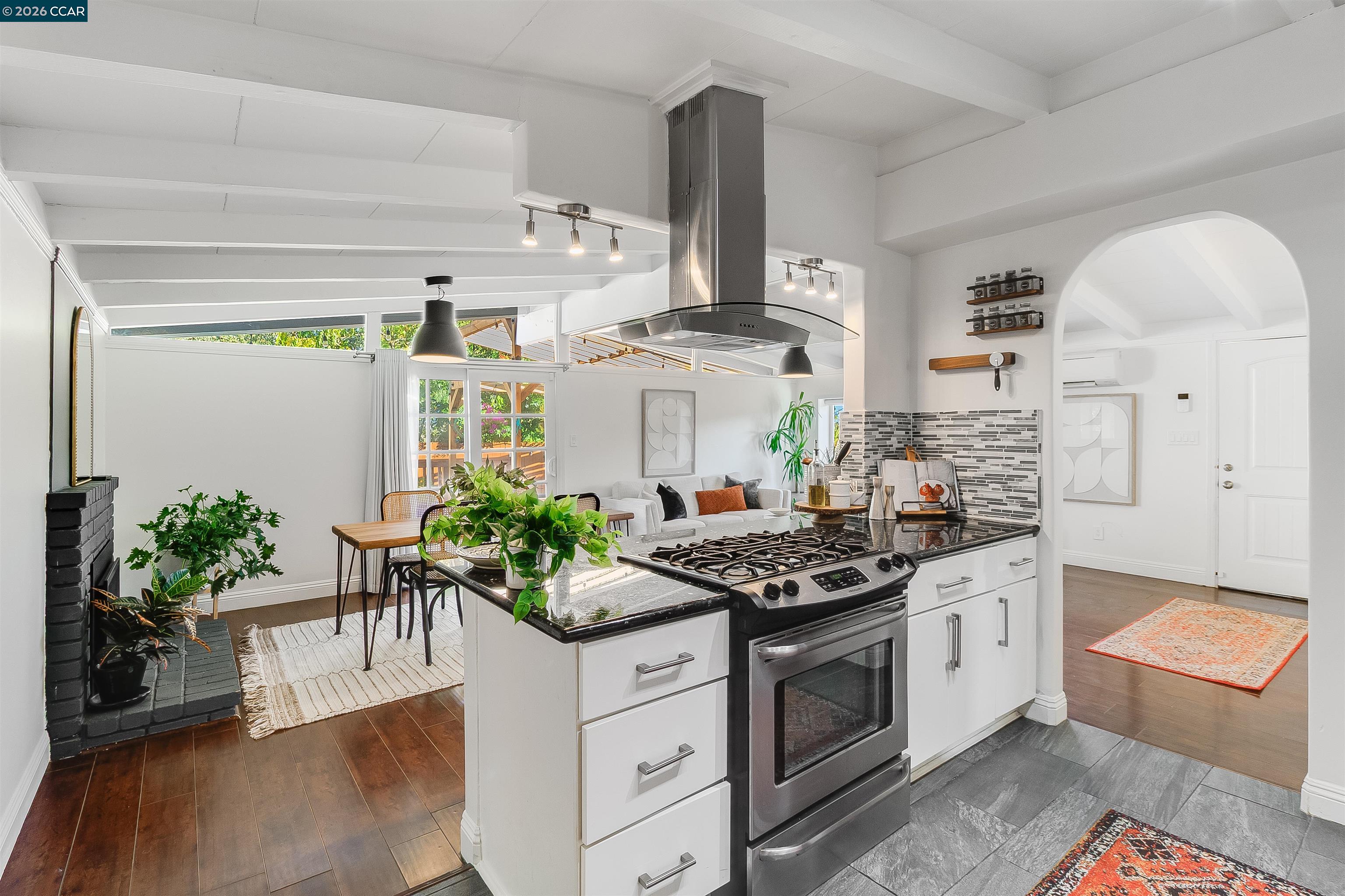 Open-plan kitchen with white cabinetry, stainless-steel range, dark counters, and adjoining dining and living areas.