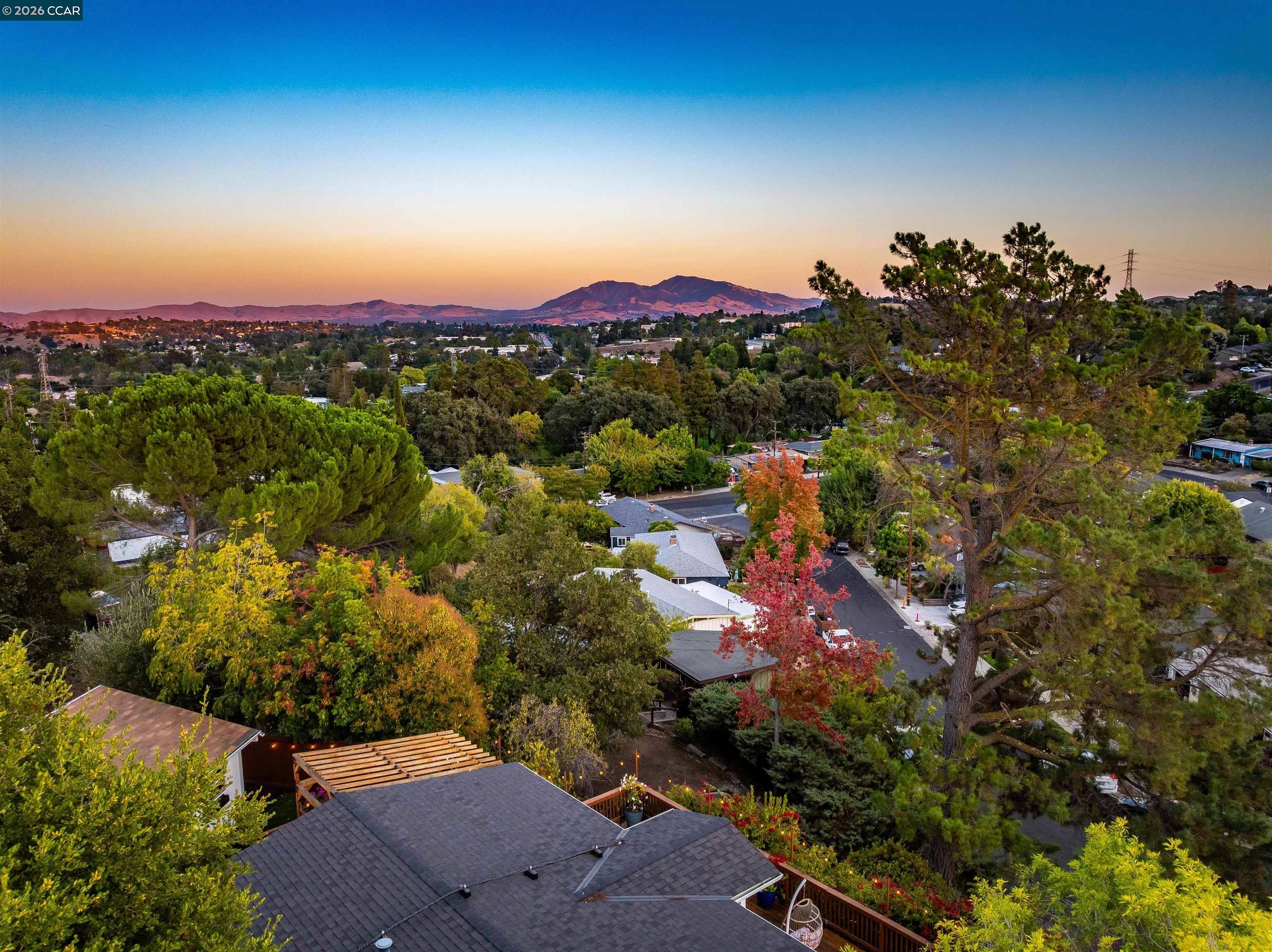 Aerial neighborhood view at sunset, with autumn trees, a foreground roof and deck, and distant mountains.