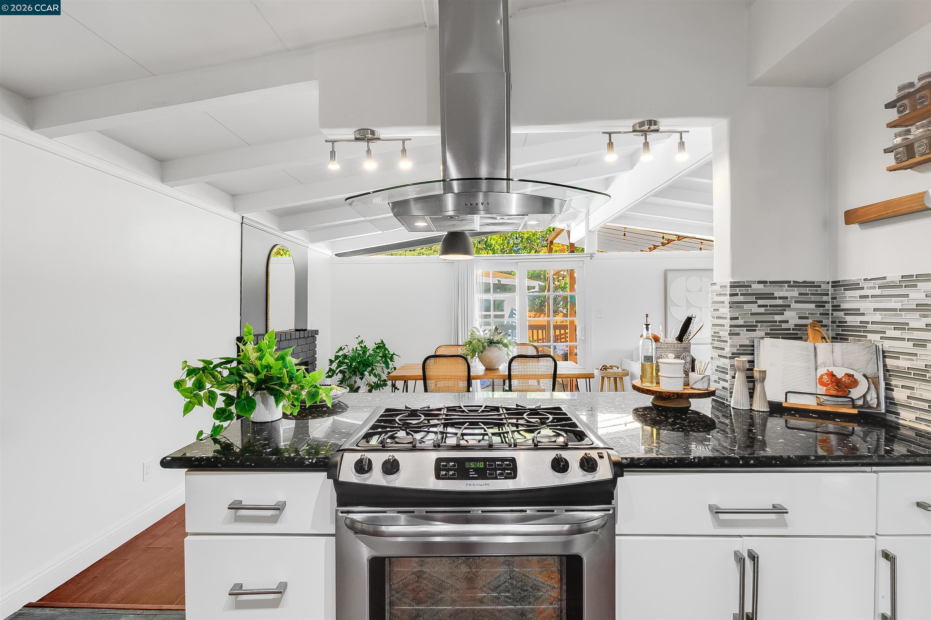 Bright kitchen with a stainless-steel range, black countertops, and an adjoining dining area.