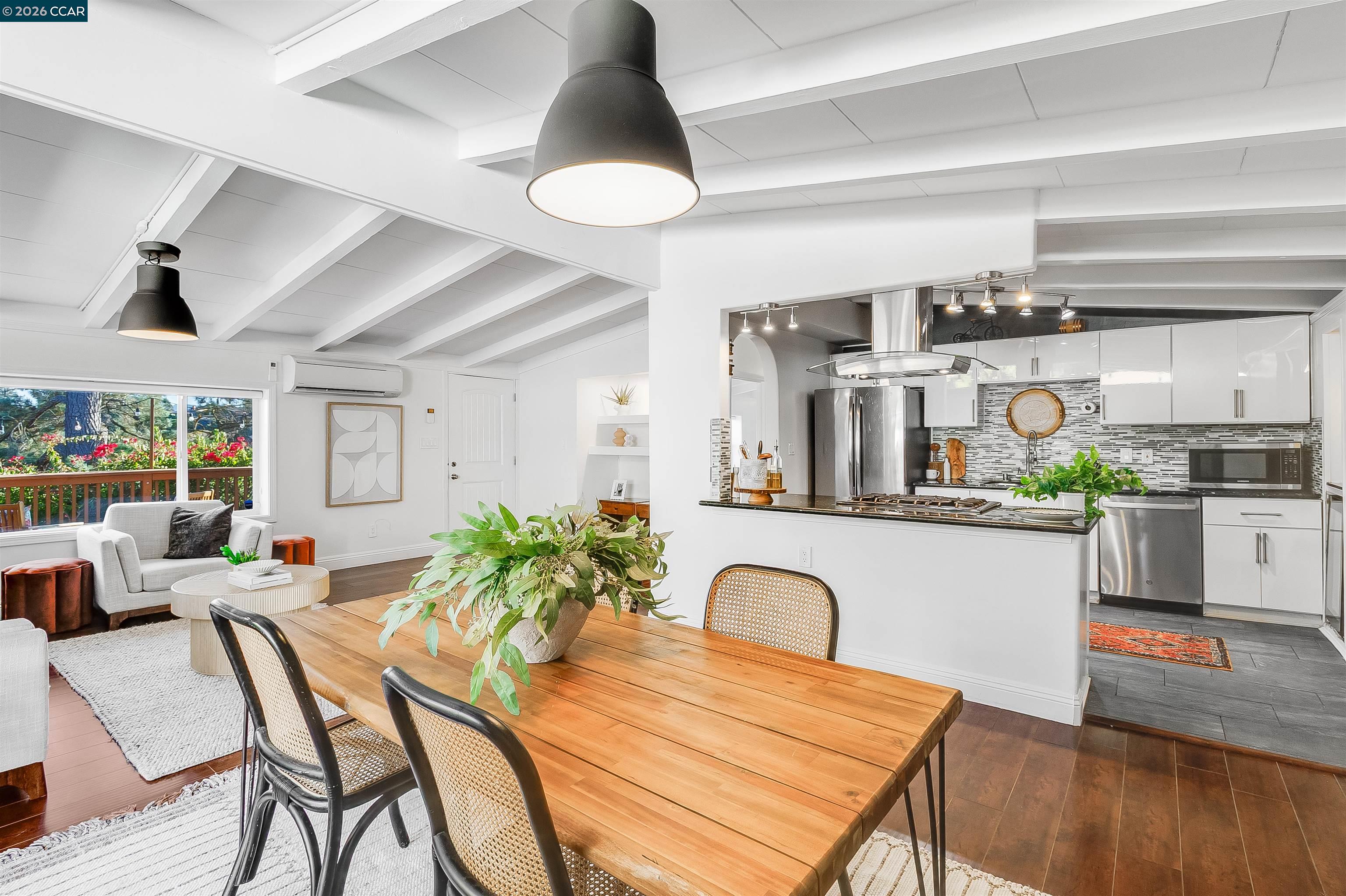 Open-plan kitchen and dining area with white cabinetry, stainless steel appliances, and exposed ceiling beams.