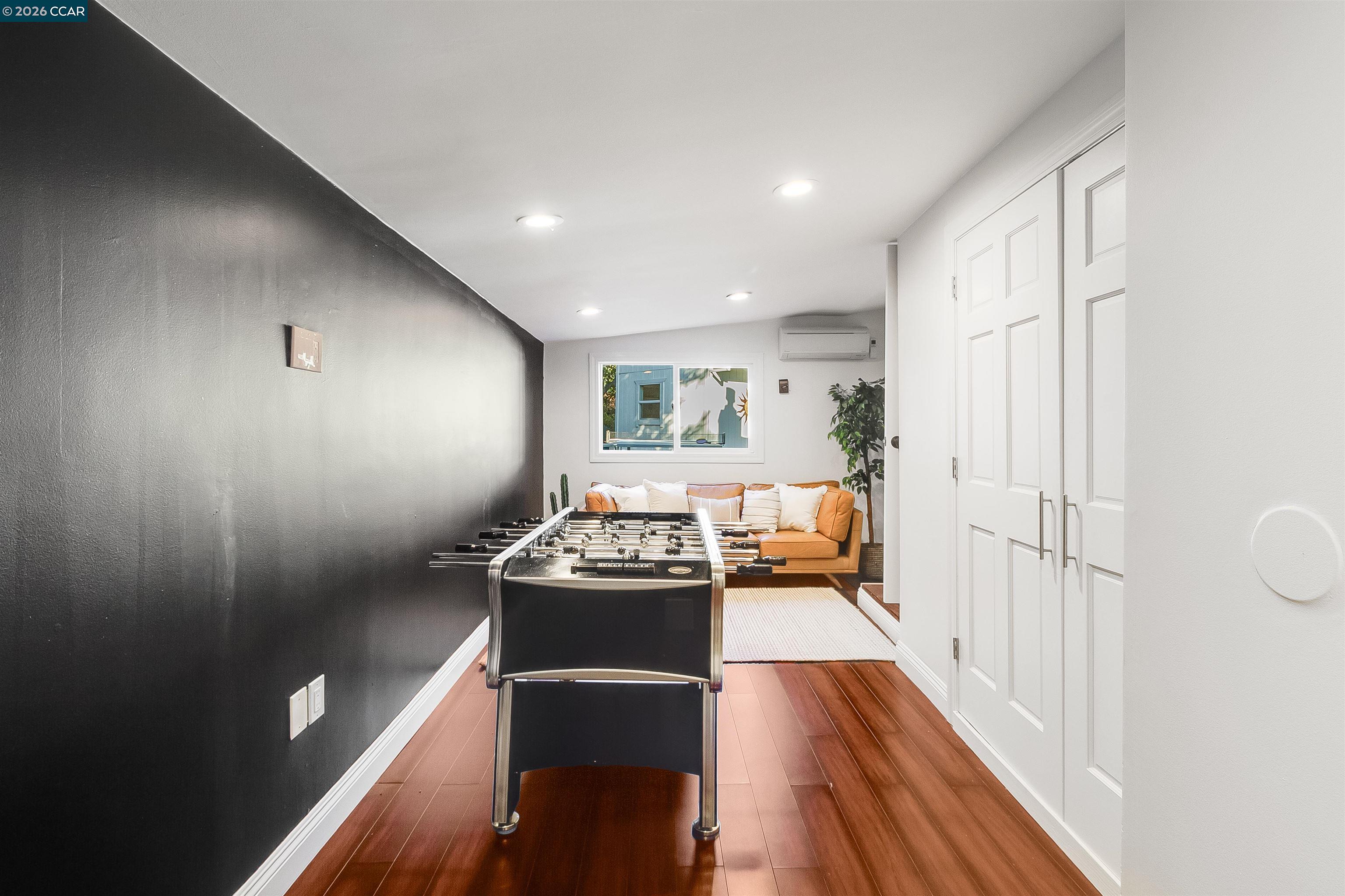 Game room with a foosball table, tan sofa, and reddish wood flooring.