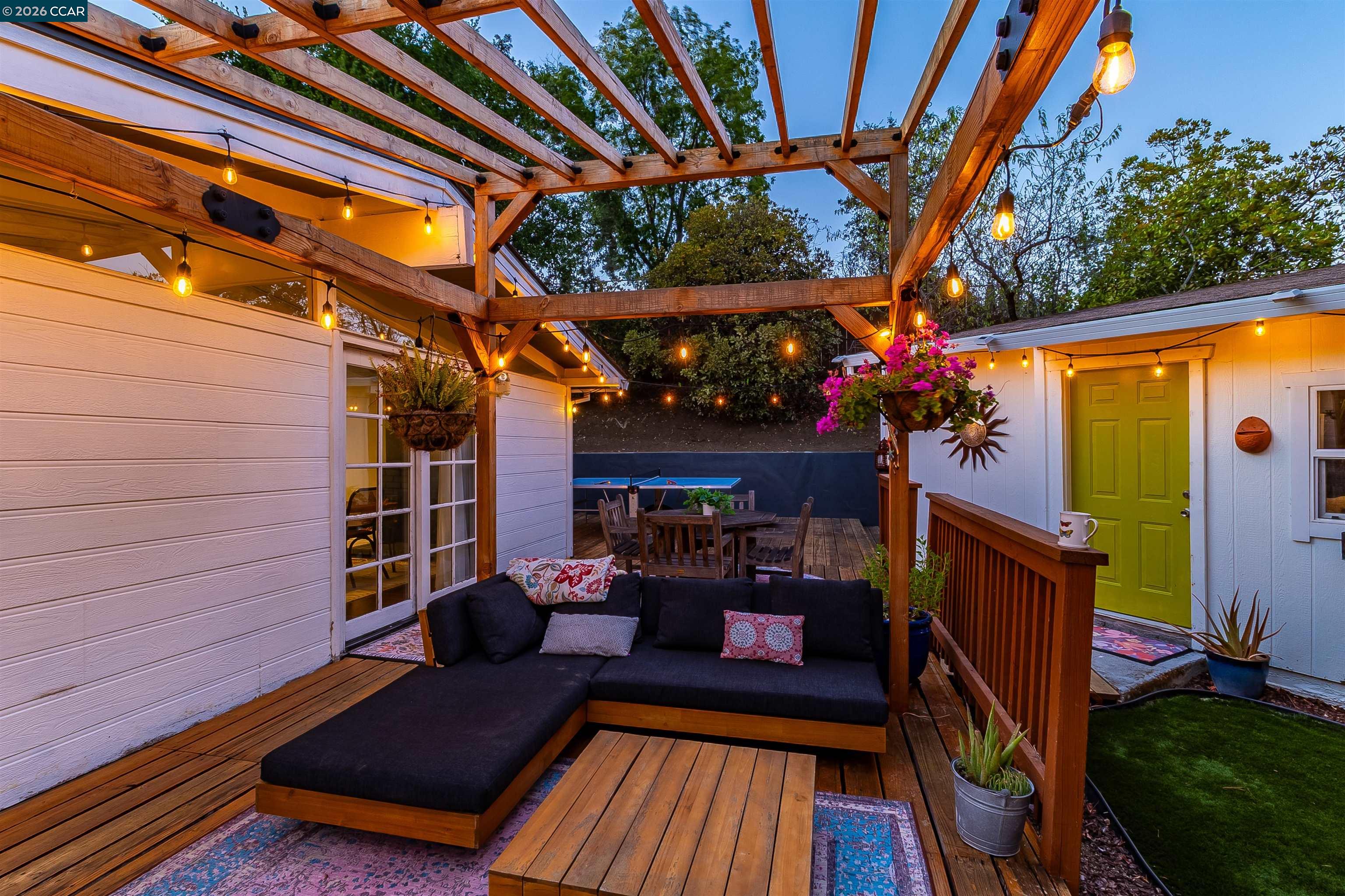 Backyard deck with a timber pergola, string lights, sectional seating, and a bright green door.