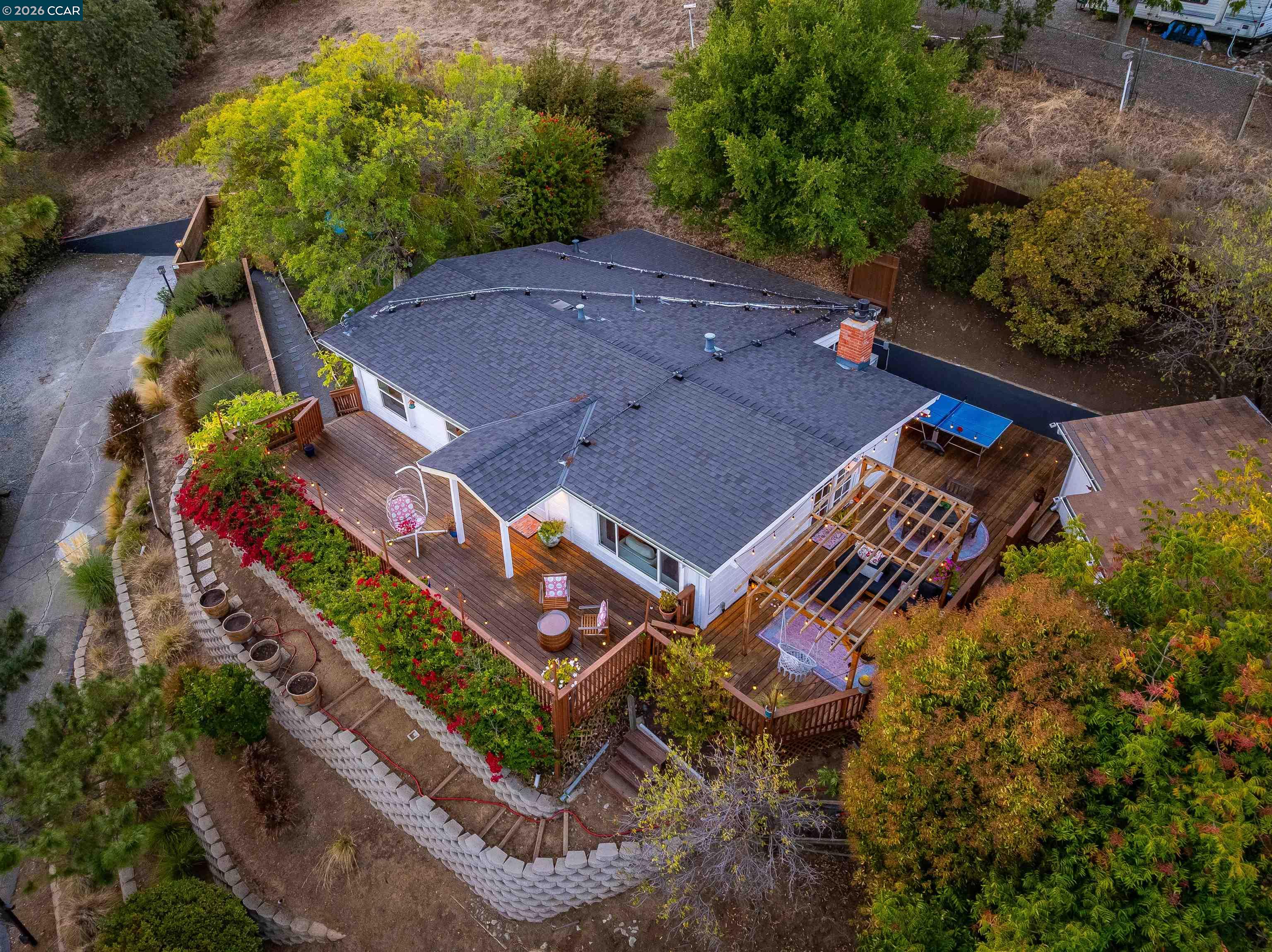 Aerial view of a home with expansive wooden decks, a pergola, and landscaped retaining walls.