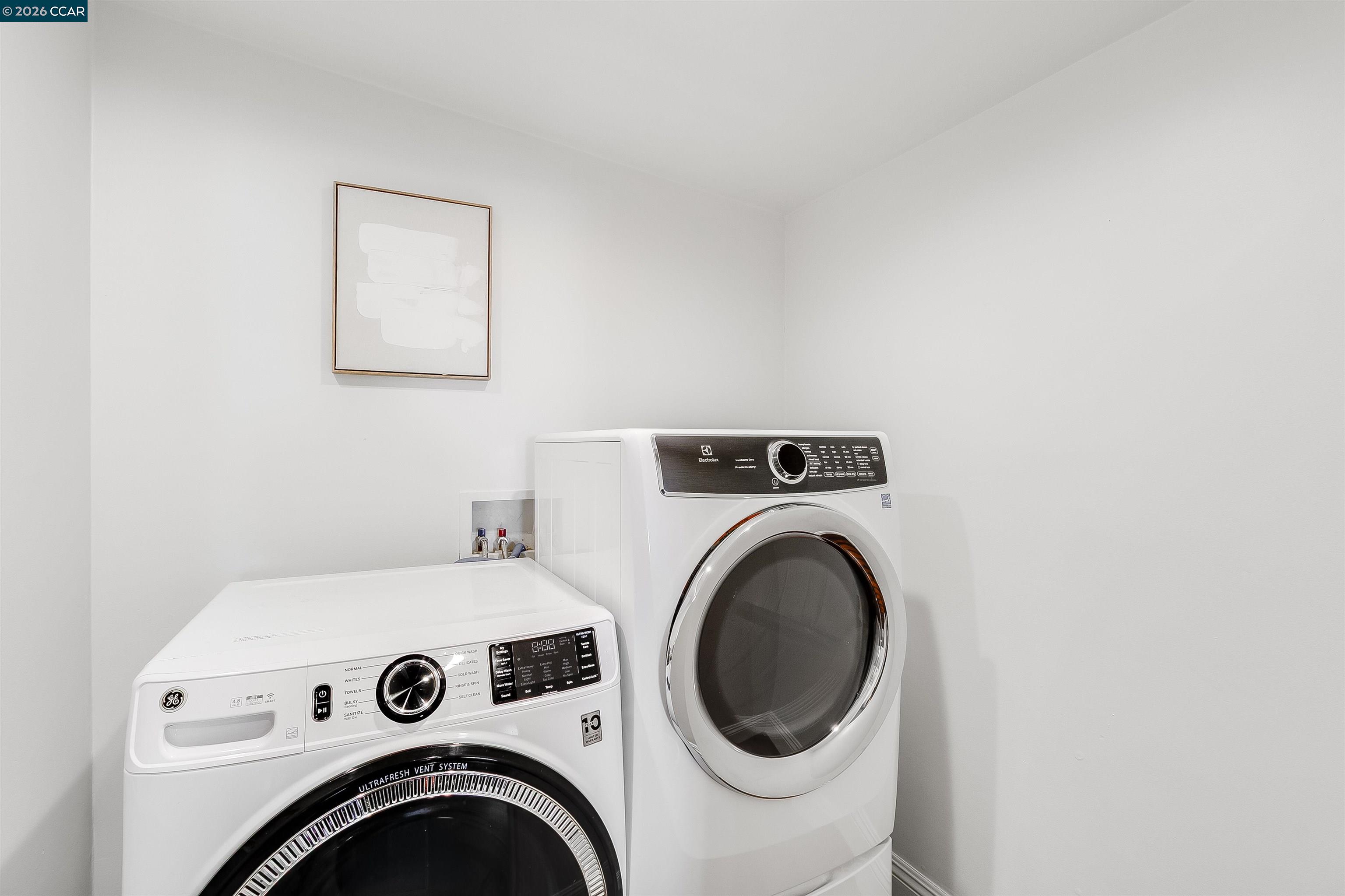 Laundry room with white front-loading washer and dryer and framed abstract art.