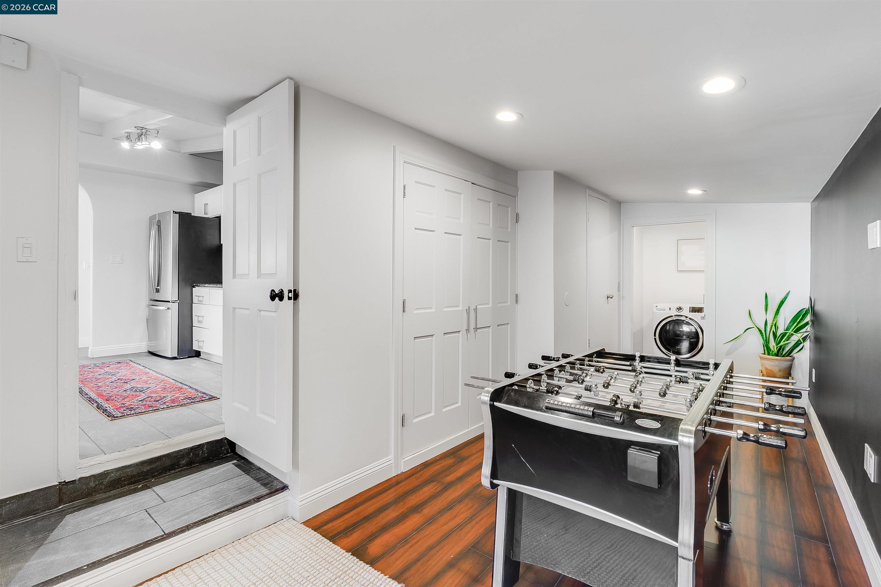Game room with a black foosball table, wood floors, and adjoining laundry area.