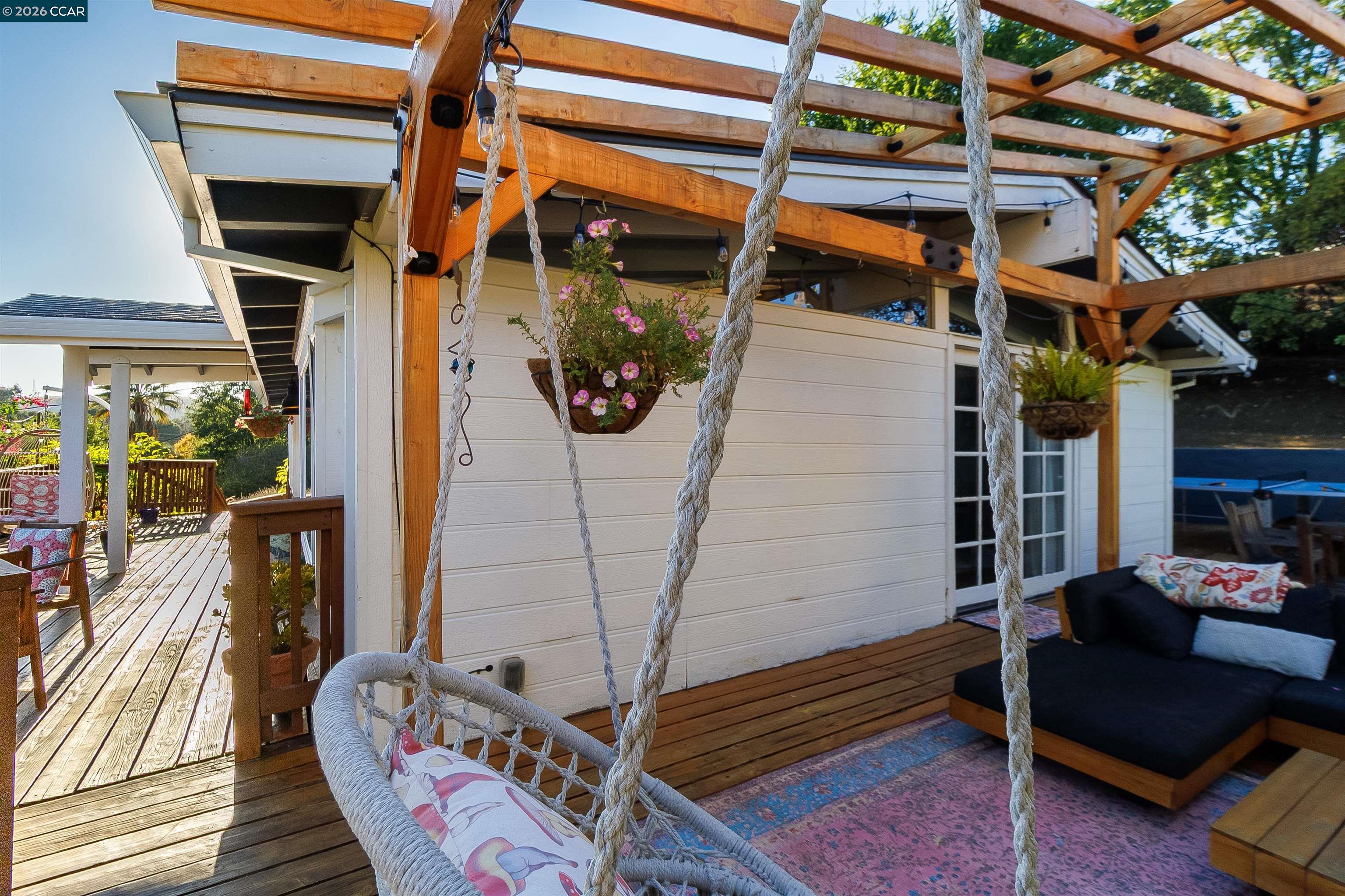Wooden deck with a timber pergola, rope swing, hanging flowers, and outdoor sofa.