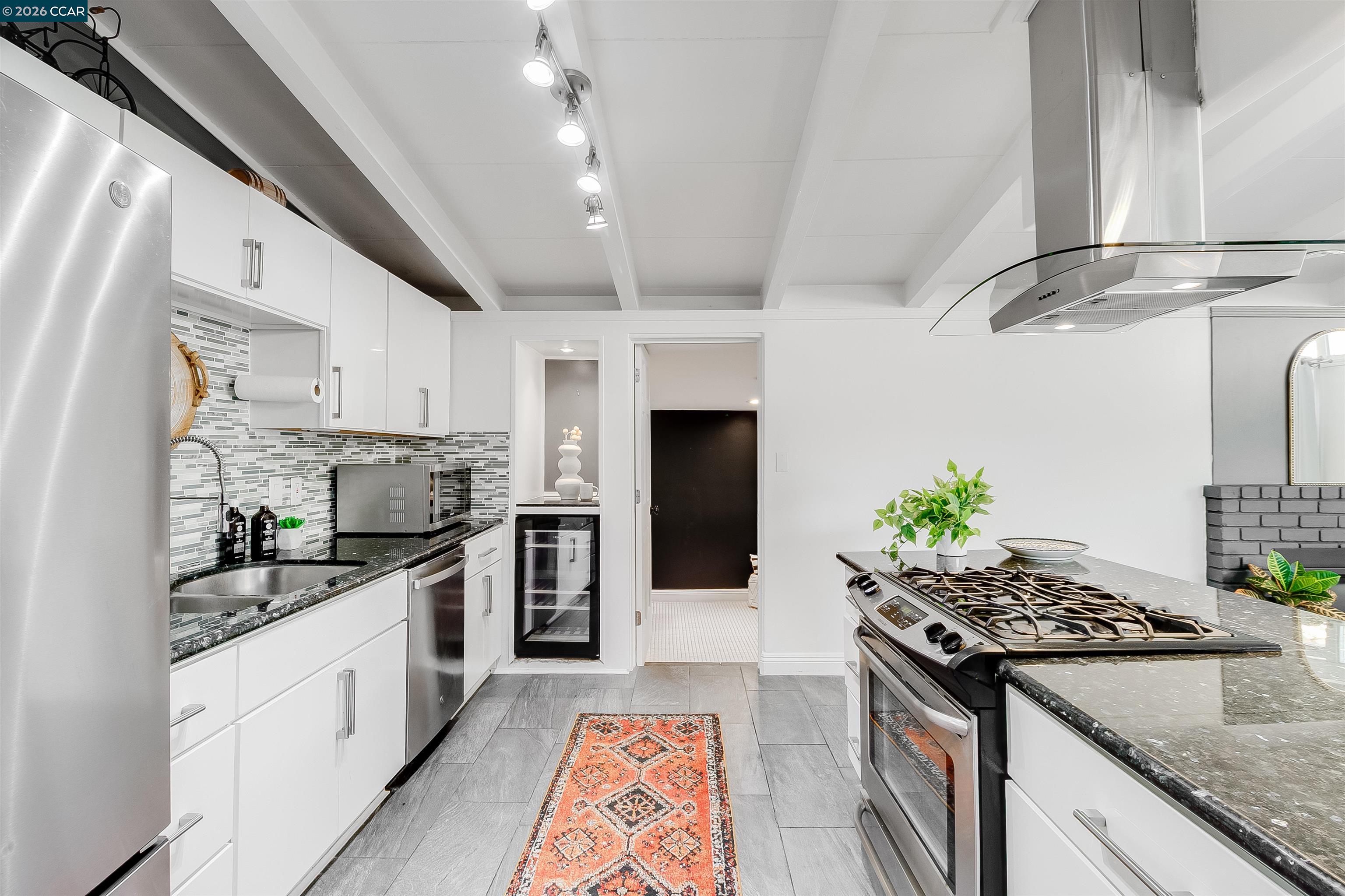 Remodeled kitchen with white cabinets, stainless appliances, a large gas range, and patterned runner rug.
