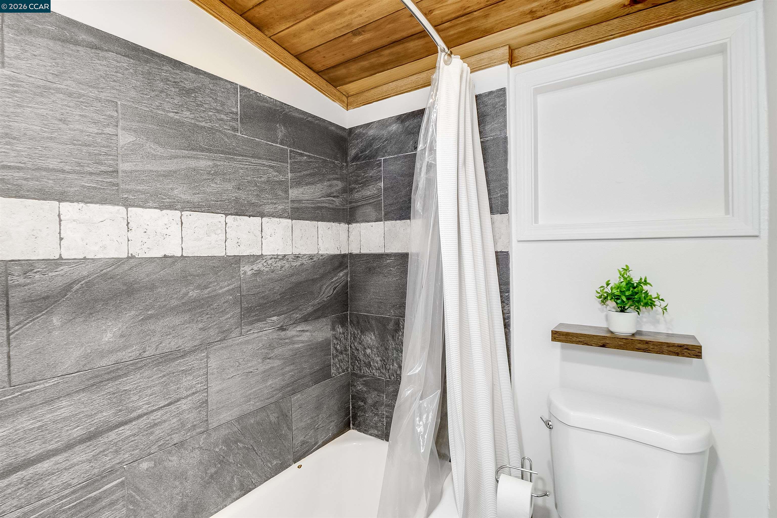 Bathroom with gray tiled shower, white bathtub, and wood-plank ceiling.