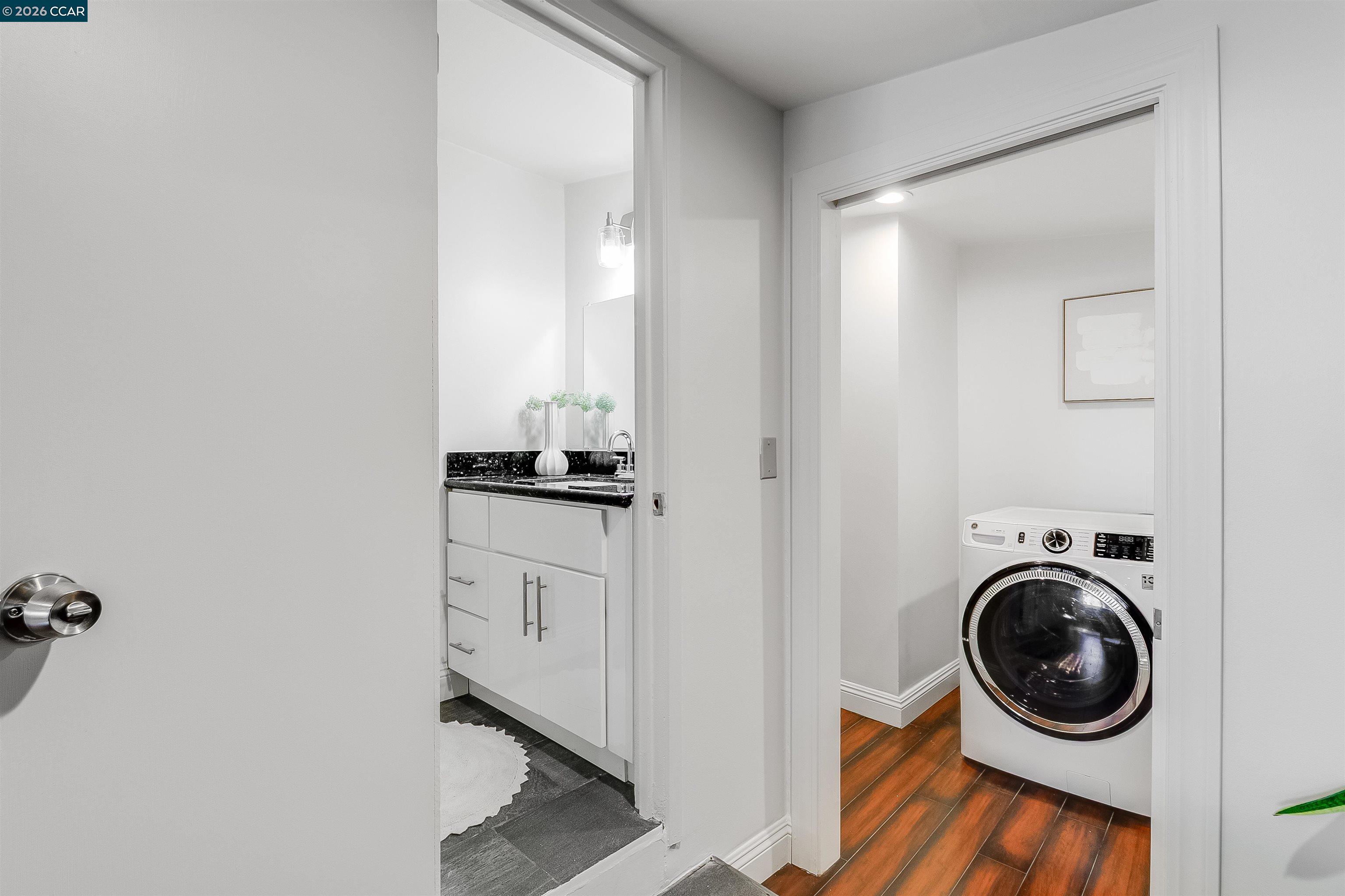 Bathroom vanity beside a laundry area with a front-loading washer and wood-look flooring.