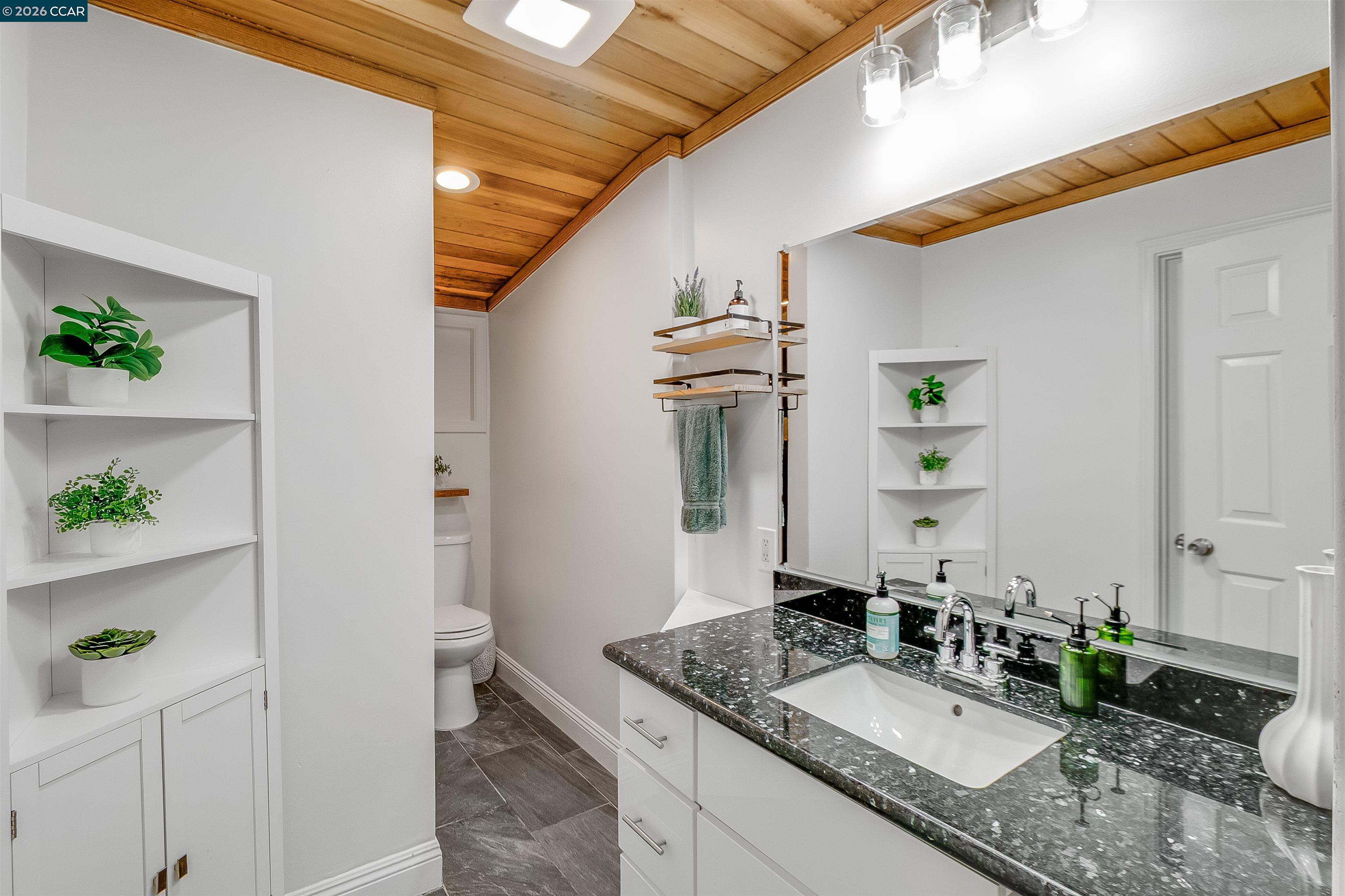 Bathroom with a speckled stone vanity, large mirror, and warm wood-plank ceiling.