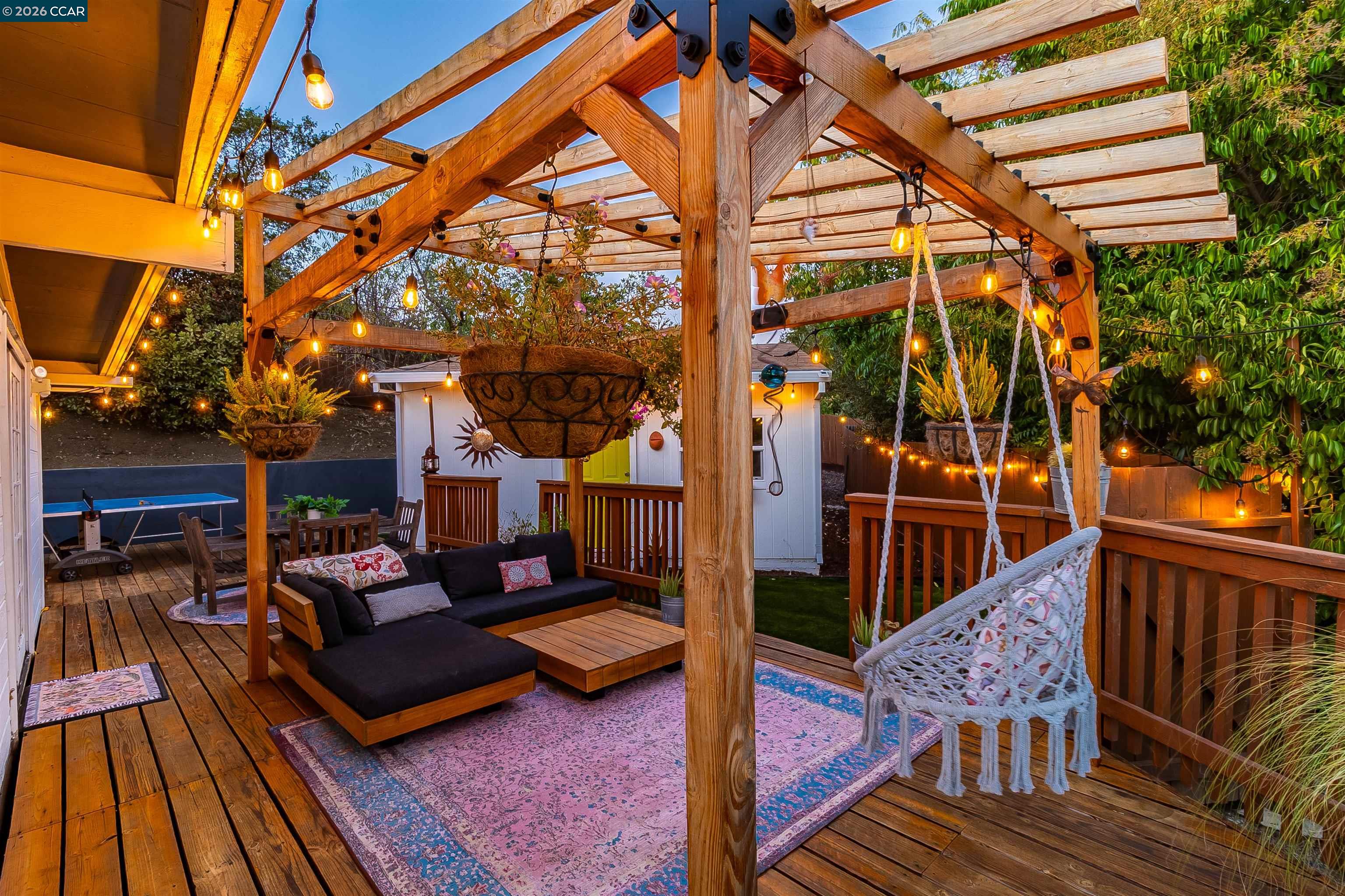 Outdoor deck beneath a timber pergola, furnished with lounge seating and a hanging chair.
