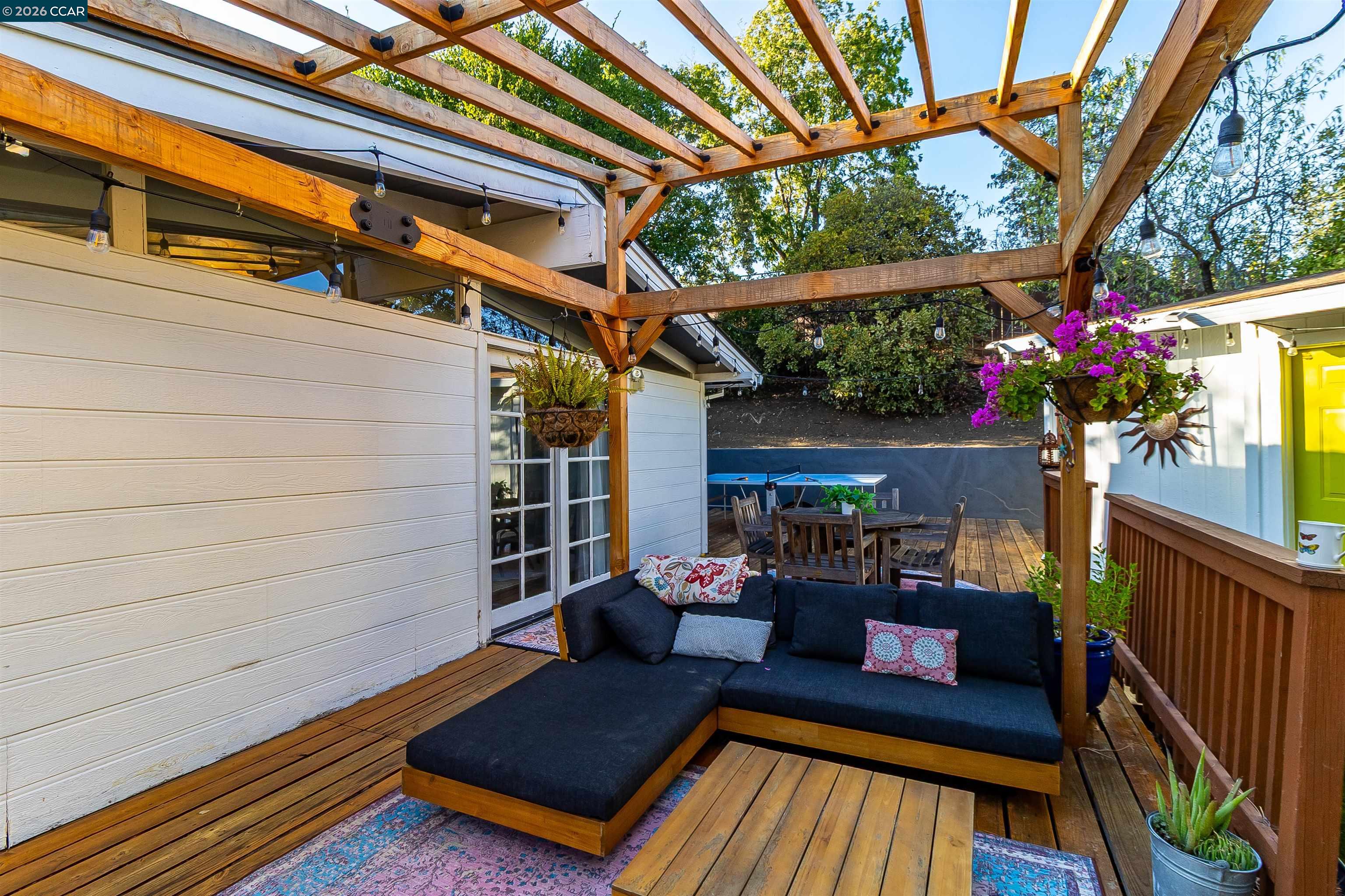 Outdoor deck with a timber pergola, string lights, and a dark sectional sofa.