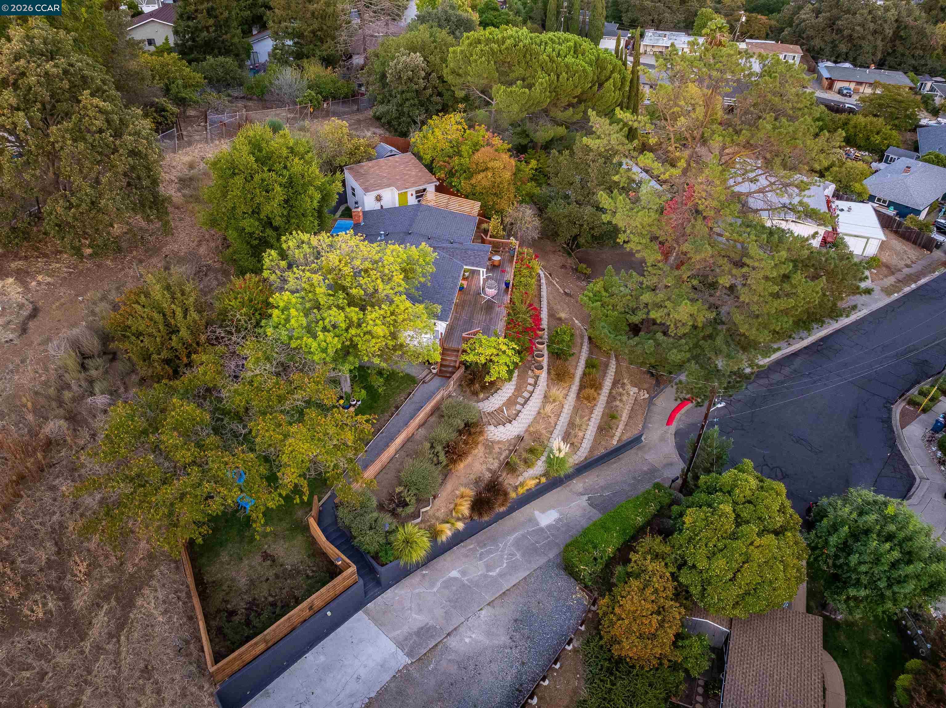 Aerial view of a home with a long deck, landscaped paths, and mature trees.