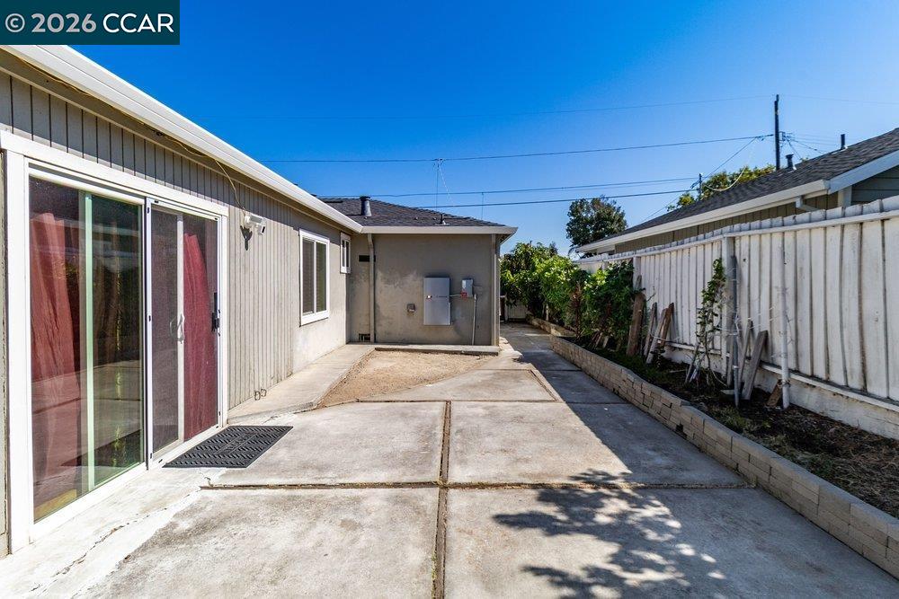 Rear concrete patio beside the home's sliding glass doors and fenced side yard.