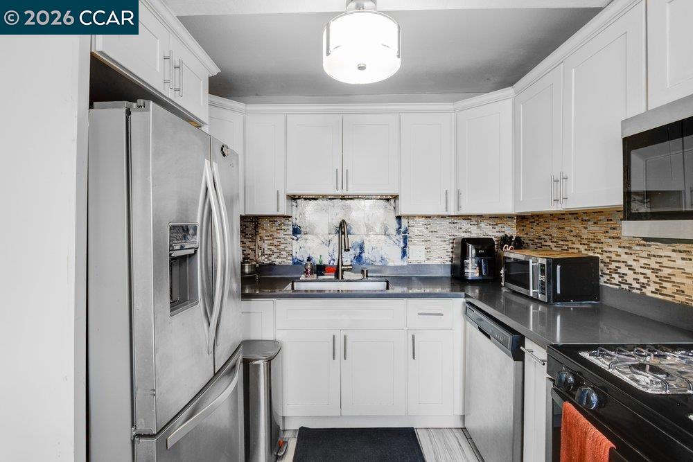 Kitchen with white cabinets, dark counters, stainless steel appliances, and a mosaic backsplash.