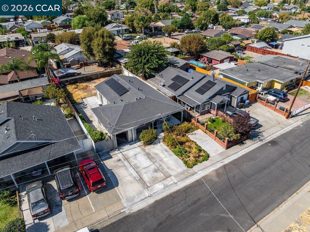 Aerial view of a single-story home with rooftop solar panels, a landscaped yard, and a driveway.