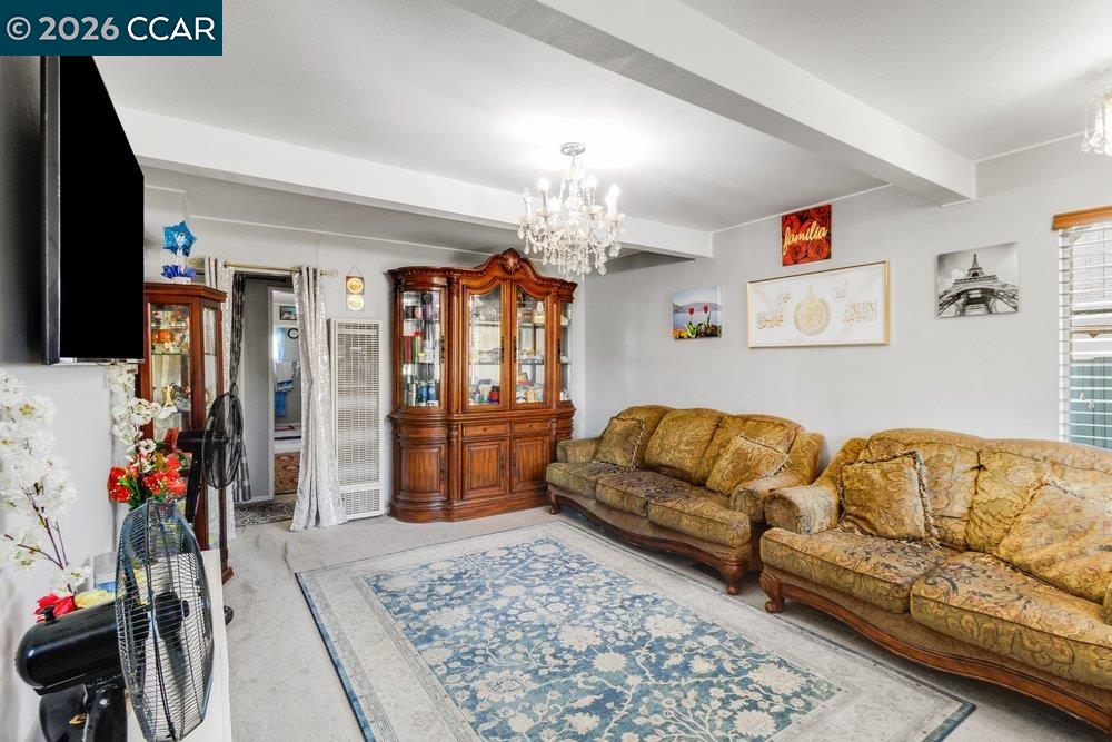 Living room with patterned sofas, ornate wood display cabinets, a blue-and-white rug, and a chandelier.