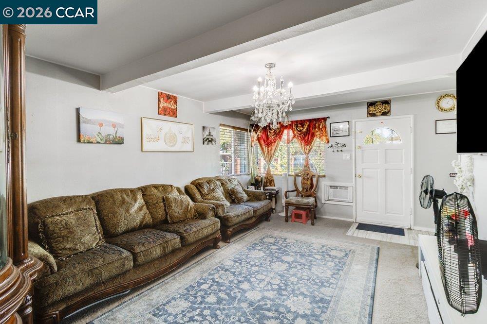 Living room with a brown patterned sectional, crystal chandelier, and red-curtained windows.