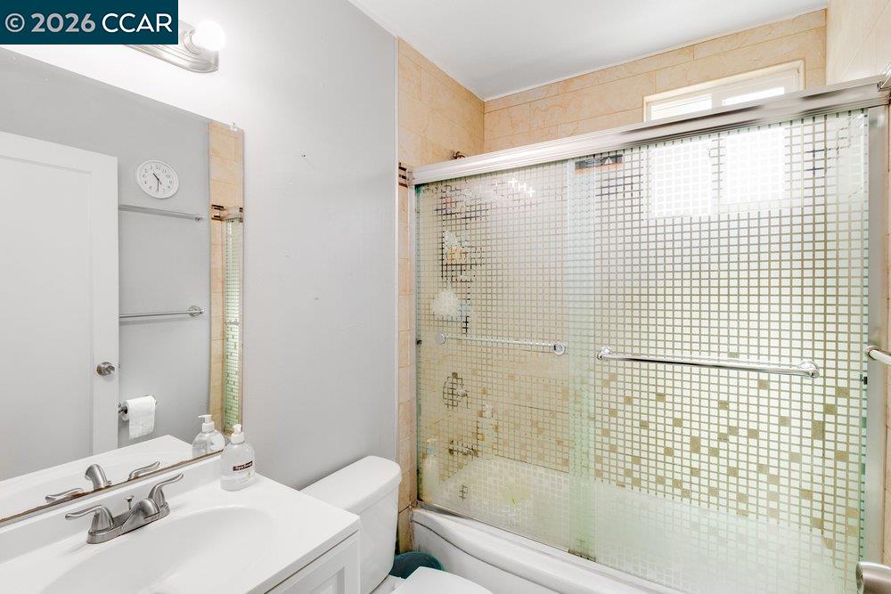 Bathroom with a white vanity and toilet beside a bathtub with patterned glass sliding doors.