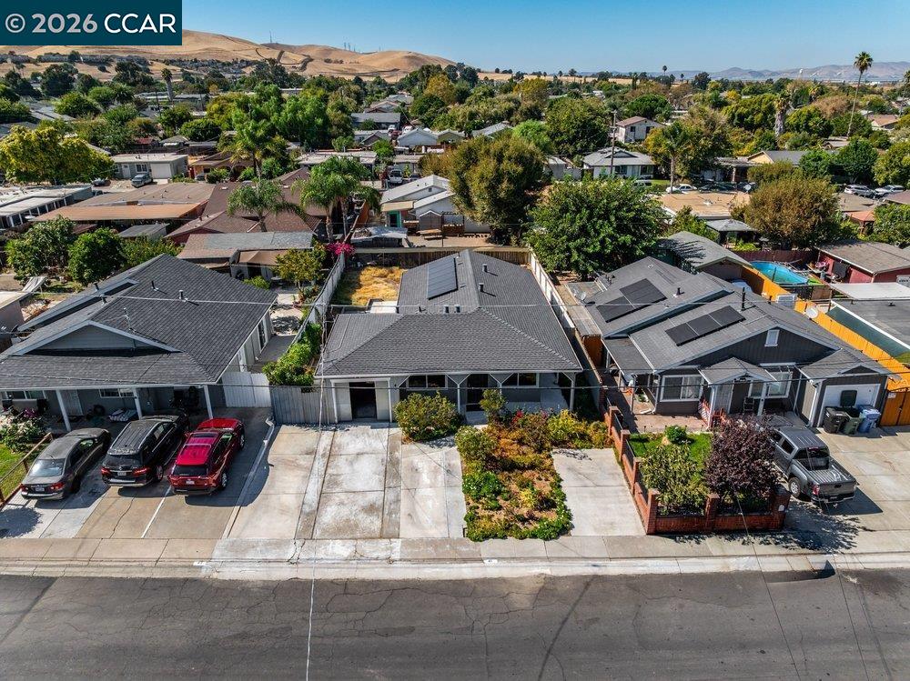 Aerial view of a gray-roofed home with solar panels, driveway, and landscaped front yard.