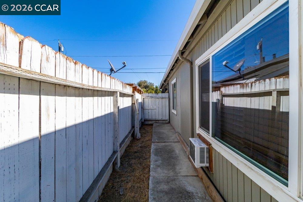 Side walkway beside the house, with a tall white fence and reflective windows.