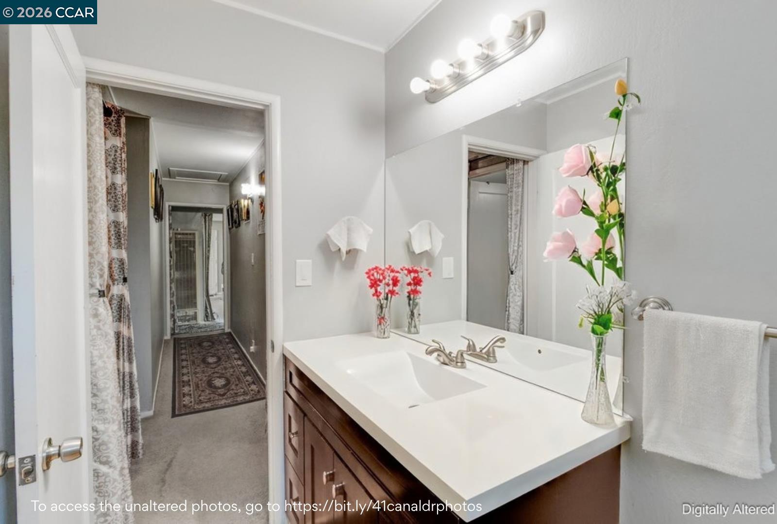 Bathroom with a double vanity, large mirror, and a hallway leading toward a shower.