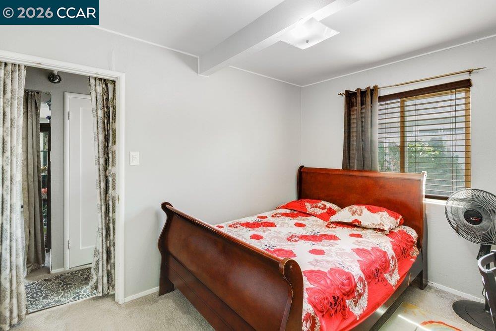 Bedroom with a dark wood bed dressed in red floral bedding beside a window with wooden blinds.