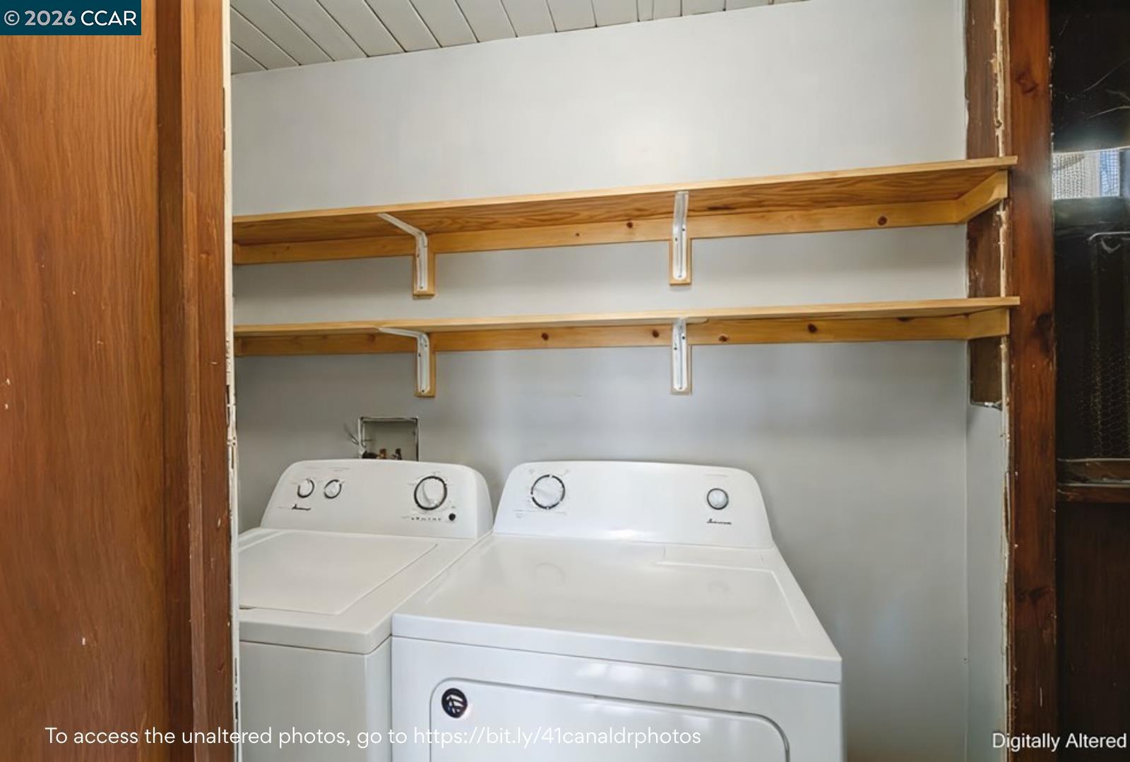 Laundry closet with a white washer and dryer beneath two wooden shelves.