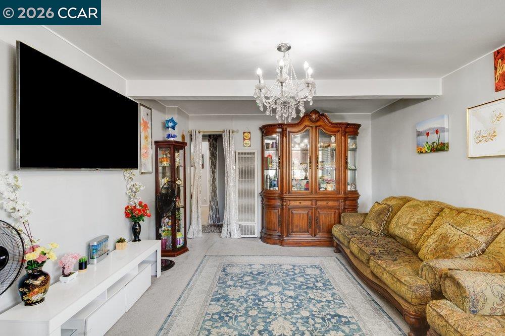 Living room with a crystal chandelier, ornate wooden cabinet, patterned sofa, and blue rug.