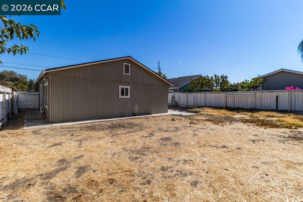 Fenced backyard with a brown detached outbuilding and dry, patchy grass.