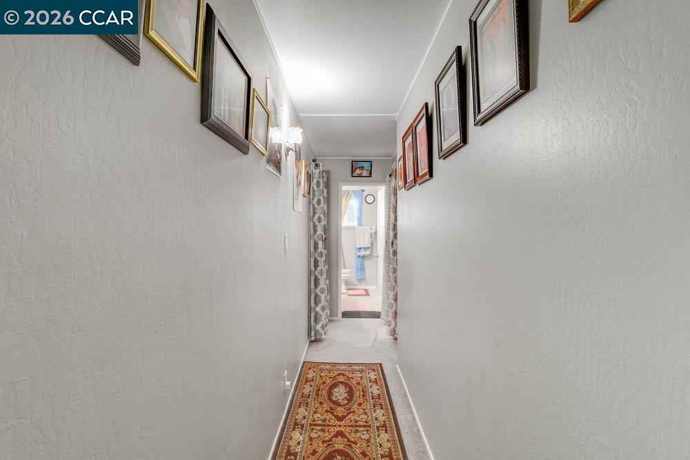 Hallway with framed pictures and a patterned runner leading to a bathroom.
