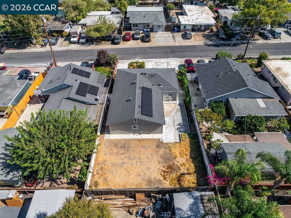 Aerial view of a home with solar panels and a large dry backyard between neighboring houses.
